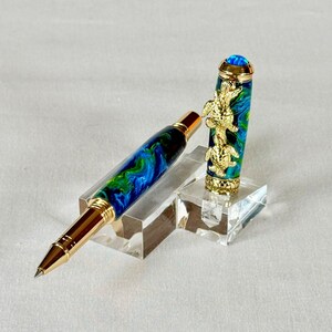 The Sea Turtle Roller Ball pen features a stunning blue-ocean synthetic Fire Opal, turtle shell texture, and sea turtle clip. Truly a turtle lover gift. It comes either as a Rollerball or Fountain Pen. The cap posts securely with wide threads that won't cross. Hawaiian Honu Pen that has beautiful ocean themed features. One of my favorite Sea Creatures is the Sea Turtle. This Pen has it all. The pen comes with a windowed pen box making this item gift-ready.