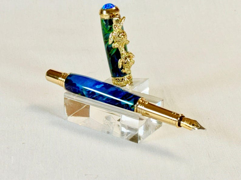 The Sea Turtle Roller Ball pen features a stunning blue-ocean synthetic Fire Opal, turtle shell texture, and sea turtle clip. Truly a turtle lover gift. It comes either as a Rollerball or Fountain Pen. The cap posts securely with wide threads that won't cross. Hawaiian Honu Pen that has beautiful ocean themed features. One of my favorite Sea Creatures is the Sea Turtle. This Pen has it all. The pen comes with a windowed pen box making this item gift-ready.