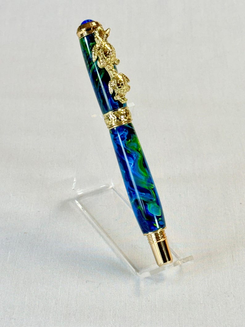 The Sea Turtle Roller Ball pen features a stunning blue-ocean synthetic Fire Opal, turtle shell texture, and sea turtle clip. Truly a turtle lover gift. It comes either as a Rollerball or Fountain Pen. The cap posts securely with wide threads that won't cross. Hawaiian Honu Pen that has beautiful ocean themed features. One of my favorite Sea Creatures is the Sea Turtle. This Pen has it all. The pen comes with a windowed pen box making this item gift-ready.