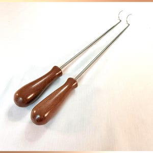 Könnte beinhalten: Zwei zahnärztliche Instrumente mit braunen Holzgriffen und Edelstahl Schäften. Die Schäfte enden in einem gebogenen Haken. Diese Werkzeuge sind für zahnärztliche Eingriffe konzipiert.