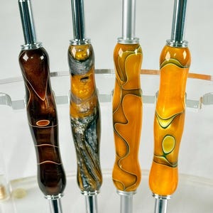 May include: Four colourful crochet hooks with silver metal tips. The hooks have a swirl pattern in shades of brown, gold, and orange.