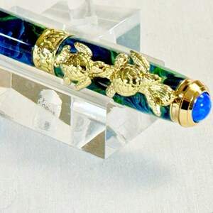 The Sea Turtle Roller Ball pen features a stunning blue-ocean synthetic Fire Opal, turtle shell texture, and sea turtle clip. Truly a turtle lover gift. It comes either as a Rollerball or Fountain Pen. The cap posts securely with wide threads that won't cross. Hawaiian Honu Pen that has beautiful ocean themed features. One of my favorite Sea Creatures is the Sea Turtle. This Pen has it all. The pen comes with a windowed pen box making this item gift-ready.