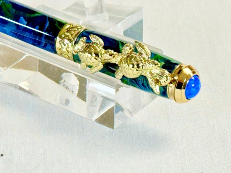 The Sea Turtle Roller Ball pen features a stunning blue-ocean synthetic Fire Opal, turtle shell texture, and sea turtle clip. Truly a turtle lover gift. It comes either as a Rollerball or Fountain Pen. The cap posts securely with wide threads that won't cross. Hawaiian Honu Pen that has beautiful ocean themed features. One of my favorite Sea Creatures is the Sea Turtle. This Pen has it all. The pen comes with a windowed pen box making this item gift-ready.