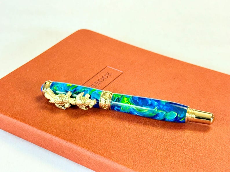 The Sea Turtle Roller Ball pen features a stunning blue-ocean synthetic Fire Opal, turtle shell texture, and sea turtle clip. Truly a turtle lover gift. It comes either as a Rollerball or Fountain Pen. The cap posts securely with wide threads that won't cross. Hawaiian Honu Pen that has beautiful ocean themed features. One of my favorite Sea Creatures is the Sea Turtle. This Pen has it all. The pen comes with a windowed pen box making this item gift-ready.