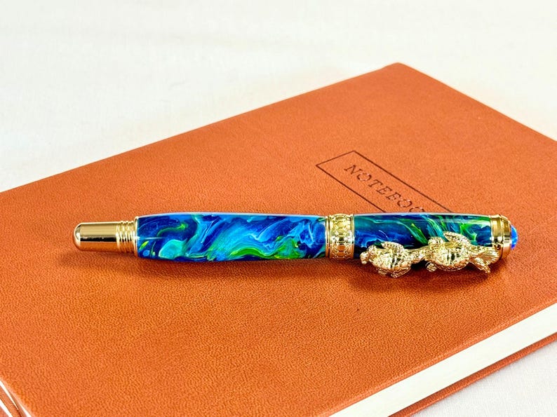 The Sea Turtle Roller Ball pen features a stunning blue-ocean synthetic Fire Opal, turtle shell texture, and sea turtle clip. Truly a turtle lover gift. It comes either as a Rollerball or Fountain Pen. The cap posts securely with wide threads that won't cross. Hawaiian Honu Pen that has beautiful ocean themed features. One of my favorite Sea Creatures is the Sea Turtle. This Pen has it all. The pen comes with a windowed pen box making this item gift-ready.