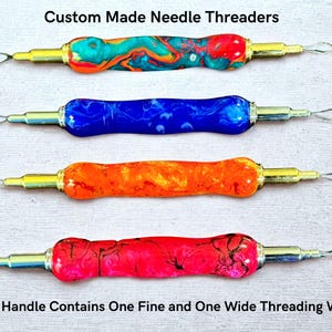 May include: Four custom-made needle threaders with colorful, swirled resin handles in teal, blue, orange, and red. Each tool has a gold-colored metal shaft and a silver wire loop for threading needles. The text reads: "Custom Made Needle Threaders" and "Each Handle Contains One Fine and One Wide Threading Wire."