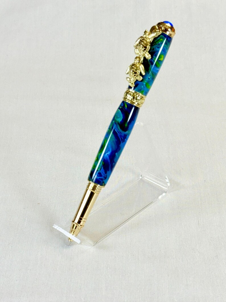 The Sea Turtle Roller Ball pen features a stunning blue-ocean synthetic Fire Opal, turtle shell texture, and sea turtle clip. Truly a turtle lover gift. It comes either as a Rollerball or Fountain Pen. The cap posts securely with wide threads that won't cross. Hawaiian Honu Pen that has beautiful ocean themed features. One of my favorite Sea Creatures is the Sea Turtle. This Pen has it all. The pen comes with a windowed pen box making this item gift-ready.