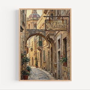 Op de afbeelding: Een ingelijst schilderij van een smalle geplaveide straat in Mdina, Malta. Het kunstwerk toont oude stenen gebouwen, een gewelfde doorgang en een bord met de tekst "Mdina". Potplanten en straatlantaarns voegen details toe aan de scène, met een koepelstructuur op de achtergrond.