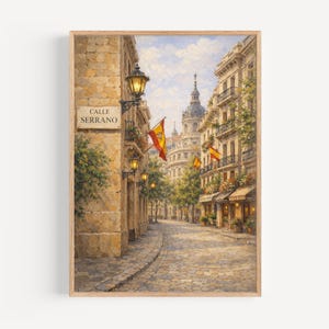 May include: A framed painting depicts a European street scene. The artwork showcases a cobblestone street lined with buildings, Spanish flags, and street lamps. The sign reads "Calle Serrano". The color palette includes warm tones of beige, brown, and yellow.