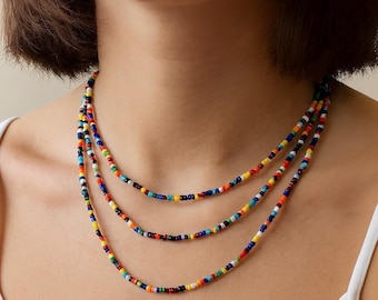 May include: A multi-strand necklace featuring small, colorful beads in a variety of colors including red, orange, yellow, green, blue, and white. The necklace is layered and worn around the neck, creating a vibrant and eye-catching accessory.
