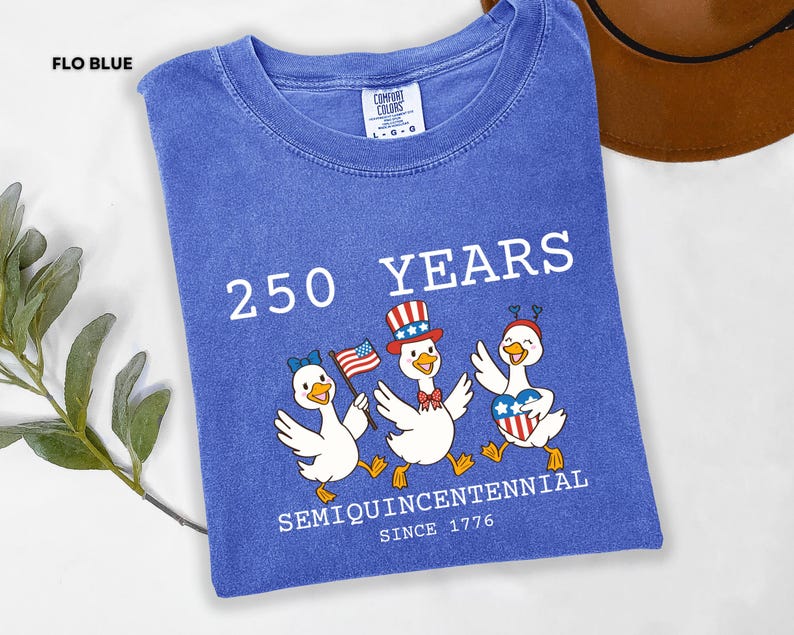 May include: Flo blue t-shirt with the text "250 YEARS SEMIQUINCENTENNIAL SINCE 1776". The shirt features a graphic of three cartoon ducks wearing patriotic accessories, including a hat, bow, and heart-shaped emblem.
