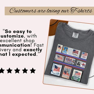 May include: A dark gray t-shirt featuring a design of vintage American postage stamps with US flags. The shirt includes the text "Customers are loving our T-shirts" and a customer review. The shirt is folded on a white surface.