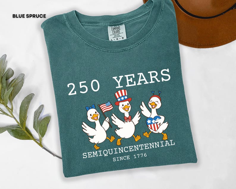May include: Blue spruce Comfort Colors t-shirt with a graphic celebrating 250 years. The design features three cartoon ducks wearing patriotic hats and holding flags. Text includes "250 YEARS" and "SEMIQUINCENTENNIAL SINCE 1776".