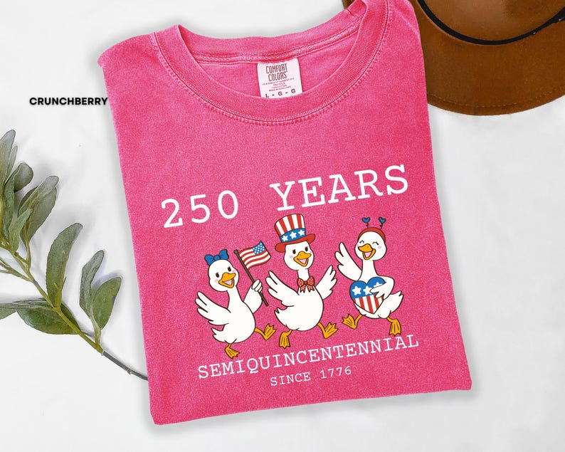 May include: A pink Comfort Colors t-shirt with the text "250 YEARS SEMIQUINCENTENNIAL SINCE 1776". The shirt features a graphic of three cartoon ducks wearing patriotic accessories and holding an American flag.