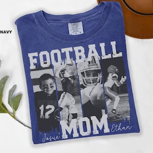 May include: A navy blue t-shirt with the words "FOOTBALL MOM" in white block letters. The shirt features a collage of black and white photos of football players. The name "Ethan" is written in script below the word "MOM". The word "TRUE NAVY" is printed on the top left.