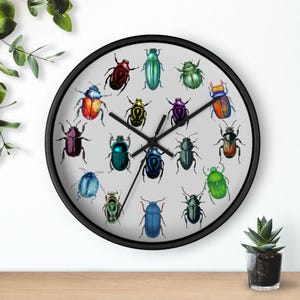 May include: A round wall clock with a black frame and a light gray face. The clock face features a collection of colorful beetle illustrations. The clock hands are black, and the clock is displayed on a wooden surface.