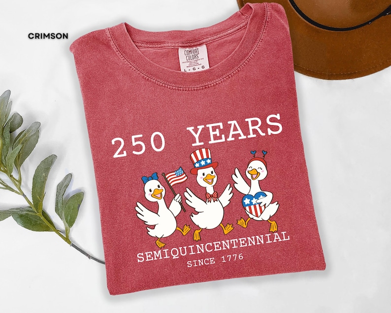 May include: Crimson red t-shirt with the text "250 YEARS SEMIQUINCENTENNIAL SINCE 1776." Features a graphic of three cartoon ducks wearing patriotic hats and holding flags. The shirt is a Comfort Colors brand.