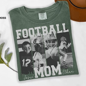 May include: Moss green t-shirt with a football-themed design. The shirt features the words "FOOTBALL MOM" in large white letters, along with black and white photos of football players. The name "Ethan" is written in script.