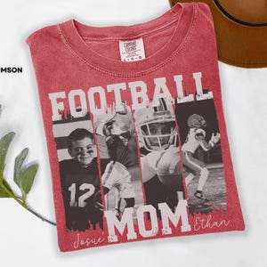 May include: Crimson red t-shirt with the words "FOOTBALL MOM" in white block letters. The shirt features a collage of black and white photos of football players. The names "Josue" and "Ethan" are written in script.