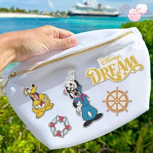 May include: White fanny pack with a gold zipper and the word "Disney DREAM" in gold lettering. The pack features cartoon character patches of Pluto, Goofy in a sailor outfit, a ship's wheel, and a life preserver.
