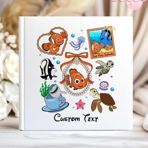 Peut inclure: Un livre photo à couverture rigide blanche avec des illustrations colorées des personnages du film "Le Monde de Nemo". La couverture présente Nemo, Dory et d'autres créatures marines, avec le texte "Custom Text" en bas.