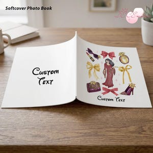 May include: Open photo book with "Custom Text" on the left page and a fashion-themed illustration on the right. The illustration includes a woman in a red dress, bows, perfume, a purse, lipstick, and high heels. The book is labeled "Softcover Photo Book".