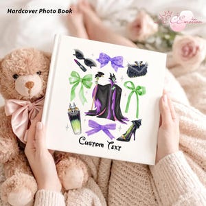 May include: A white hardcover photo book with a colorful illustration featuring a villain character, bows, and accessories. The book has the text "Hardcover Photo Book" at the top and "Custom Text" at the bottom. The book is held by a person.