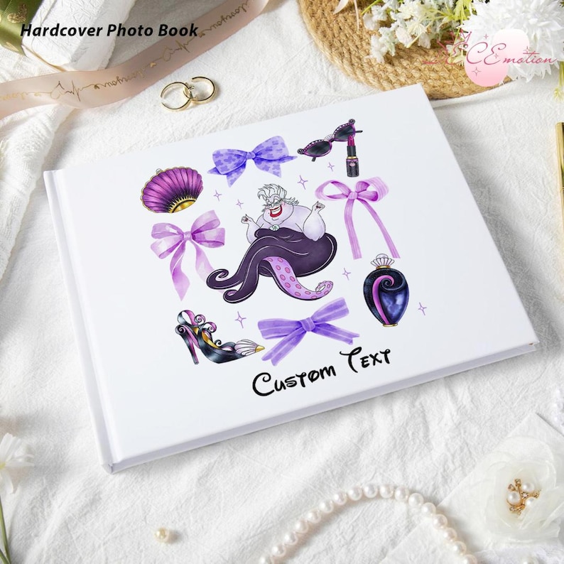 May include: White hardcover photo book with illustrations of a purple sea shell, bows, Ursula the sea witch, and other themed graphics. The text "Custom Text" is written in black script. The words "Hardcover Photo Book" are at the top.