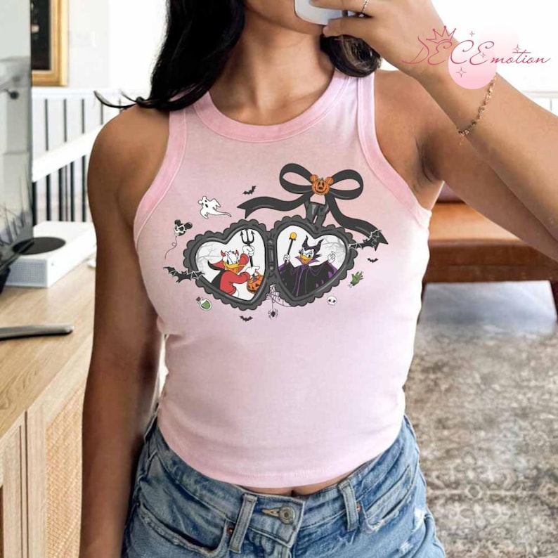 Puede incluir: Camiseta sin mangas rosa claro con ribete rosa claro. Presenta un dise&ntilde;o de Halloween con dos marcos en forma de coraz&oacute;n, personajes de dibujos animados, murci&eacute;lagos y un lazo negro con una calabaza.