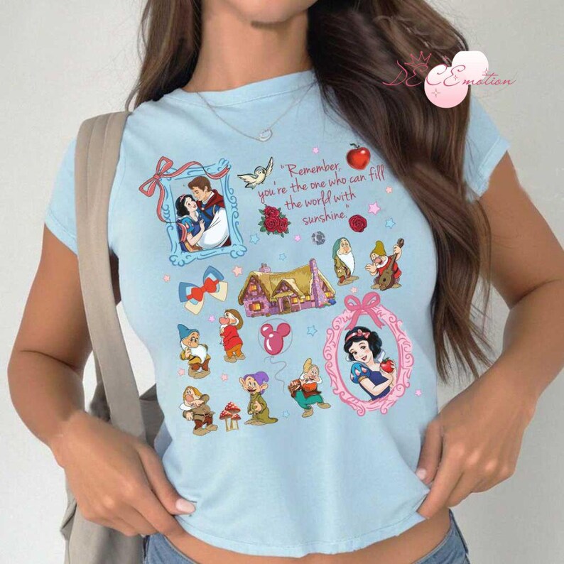 Pode incluir: Camiseta azul claro com uma estampa de Branca de Neve e os Sete An&otilde;es. A estampa inclui uma citaat: "Lembre-se, voc&ecirc; &eacute; quem pode encher o mundo de sol."