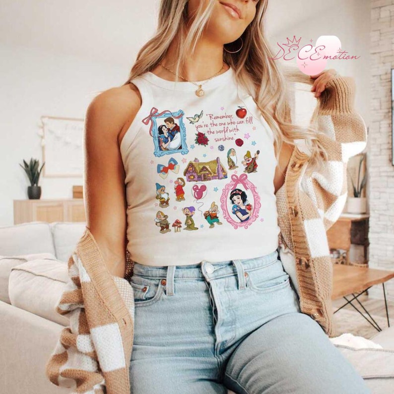 Pode incluir: Camisola branca de al&ccedil;as com uma estampa gr&aacute;fica da Branca de Neve e os Sete An&otilde;es. A estampa inclui uma citaat: "Lembre-se, voc&ecirc; &eacute; quem pode encher o mundo de sol."