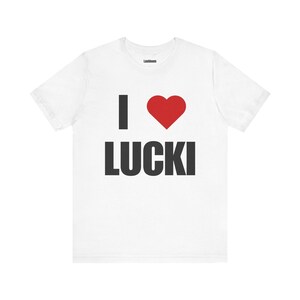 May include: White t-shirt with the text "I ♥ LUCKI" in black and a red heart. The brand name "Lushloom" is printed at the top of the shirt. The shirt is made of a soft material.