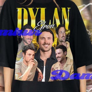 Può includere: T-shirt nero con una grafica dorata di Dylan Efron e la scritta "DYLAN Efron". Il design incorpora più immagini di Dylan Efron. Lo sfondo ha un effetto sfocato con fulmini.