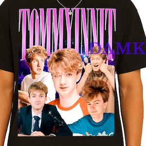 May include: Black t-shirt featuring a collage of images and the text "TOMMYINNIT" in a pink and purple gradient. The collage includes multiple images of a young man with blonde hair and various expressions. The shirt is worn by a person.