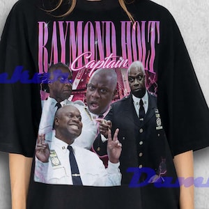 May include: Black t-shirt featuring a collage of images and the text "RAYMOND HOLT Captain" in pink and white. The images depict a bald Black man in various poses, wearing a police uniform and a suit.