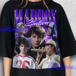 May include: Black t-shirt featuring a graphic of Maddox Batson with a purple and white design. The design includes the name "Maddox Batson" in a stylized font and multiple images of the person. The shirt is worn by a person.