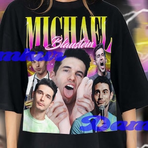 May include: Black t-shirt featuring a collage of images and the name "MICHAEL Blaustein" in a gradient yellow and pink font. The shirt has a vintage, retro style with a blurred background.