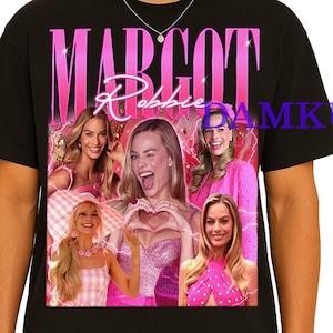 May include: Black t-shirt featuring a pink graphic with the name "Margot Robbie" and images of the actress. The design includes multiple photos of Margot Robbie in various poses and outfits, with a pink and purple color scheme.