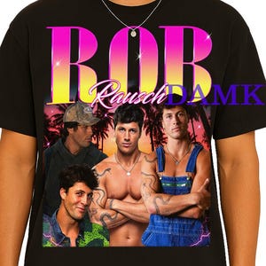 Puede incluir: Camiseta negra con un gráfico de cuatro hombres y la palabra "ROB" en letras grandes rosas y amarillas. La camiseta tiene una estética vintage, con el texto "Rausch DAMKUR" en cursiva.