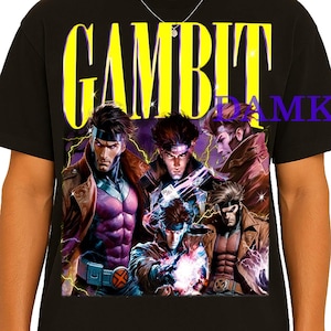 Pode incluir: Camiseta preta com um gráfico do personagem Gambit dos quadrinhos X-Men. A palavra "GAMBIT" é impressa em amarelo acima da imagem. A imagem mostra Gambit em várias poses de ação, em estilo de quadrinhos.