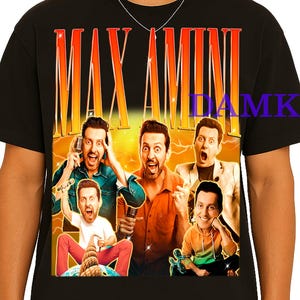 Peut inclure: T-shirt noir avec un graphisme d'un groupe d'hommes et le texte "MAX AMINI" dans une police orange et jaune dégradée. Le graphisme montre les hommes dans diverses poses, certains tenant des microphones.