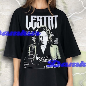 Puede incluir: Camiseta negra de gran tamaño con un gráfico de una persona y el texto blanco "LESTAT", "The Vampire" y "World Tour". La camiseta también incluye las frases "Why the long face" y "My pretty baby!"
