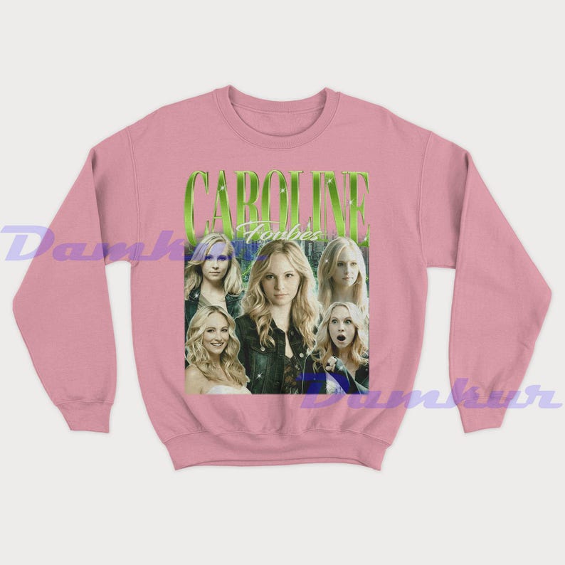 May include: Pale pink sweatshirt with a graphic of Caroline Forbes and the text "CAROLINE Forbes" in green. The graphic features multiple images of a blonde woman. The sweatshirt is a solid pale pink colour.