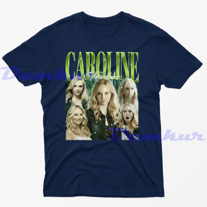 May include: A navy blue t-shirt with a graphic of a woman with blonde hair, and the text "CAROLINE Forbes" in green. The graphic includes multiple images of the woman. The shirt is made of a soft material.