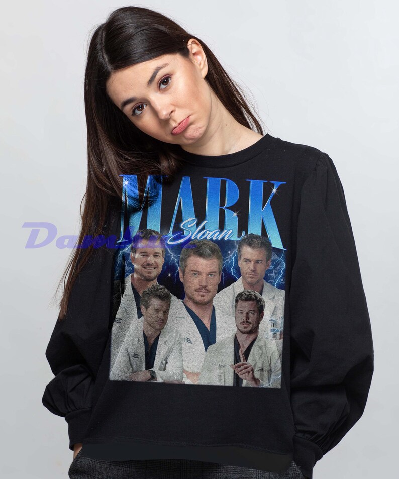K&ouml;nnte beinhalten: Schwarzes Sweatshirt mit einem Aufdruck von Mark Sloan und dem Text "MARK Sloan" in Blau und Wei&szlig;. Das Design zeigt mehrere Bilder der Figur. Das Sweatshirt hat einen Rundhalsausschnitt.