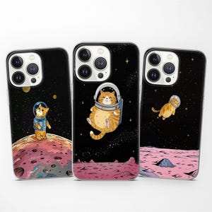 May include: Three iPhone cases with a space theme. Each case features a different illustration of a cat in a spacesuit. The first case has a cat in a blue spacesuit, the second case has a cat in a yellow spacesuit, and the third case has a cat in a red spacesuit.