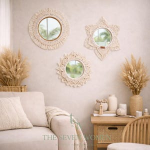 May include: Three cream-coloured wall mirrors with macramé detailing. The mirrors are in round, star, and sunburst shapes. The mirrors have a natural, bohemian aesthetic. They are hung on a neutral-coloured wall, creating a stylish display.