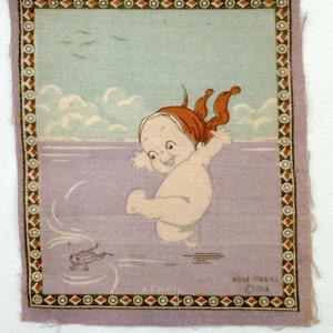 May include: A vintage fabric patch with a cartoon image of a baby in a red bandana jumping into a body of water. A small fish swims below the baby. The patch has a light blue background with white clouds and a purple border with a brown and white geometric pattern.