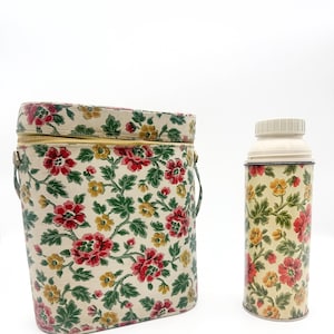 May include: A structured, oval-shaped carrying case with a zipper closure and a matching cylindrical thermos, both featuring a cream-colored background with a repeating floral pattern of red roses, yellow blossoms, and green leaves.