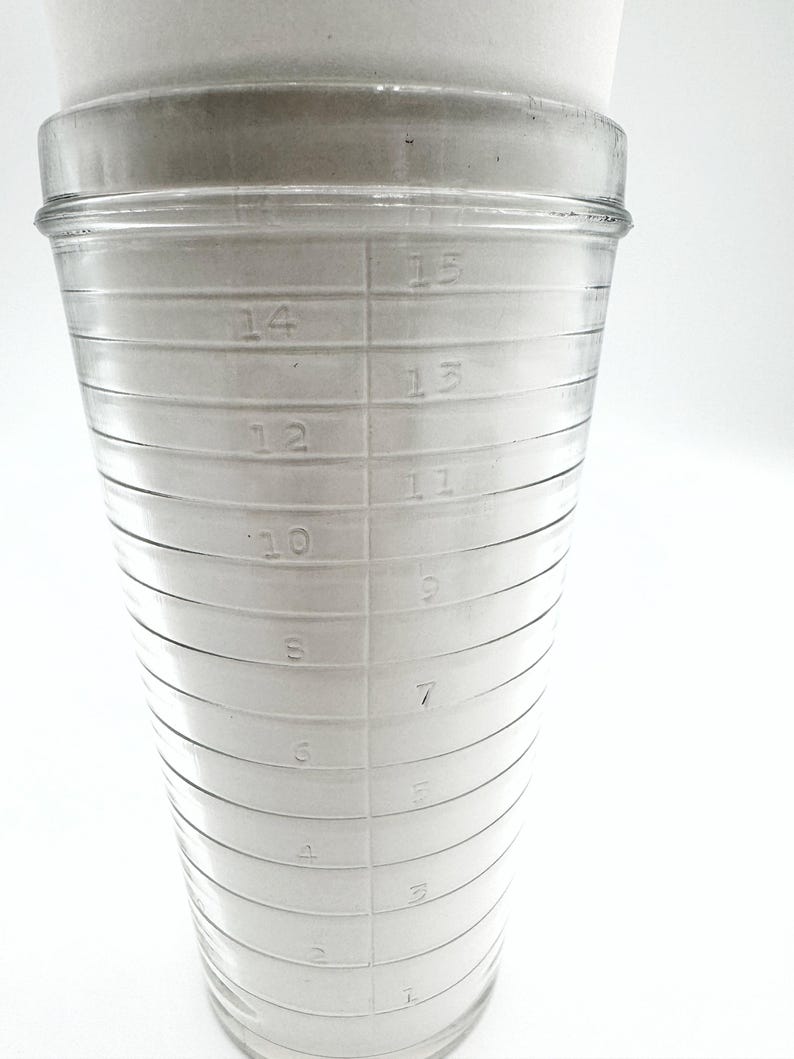 Op de afbeelding: Een doorzichtige glazen maatbeker met ge&euml;tste markeringen voor vloeistofvolume. De beker heeft een brede, cilindrische vorm met horizontale lijnen die metingen van 1 tot 15 aangeven. De cijfers zijn duidelijk zichtbaar.